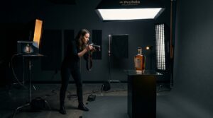 Photographer capturing a subject in a controlled studio setup with soft lighting, deep shadows, and subtle yellow accent lights defining the scene.